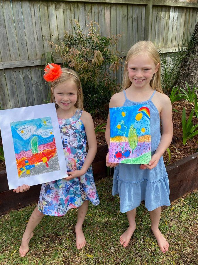 Two children proudly holding their paintings in the garden